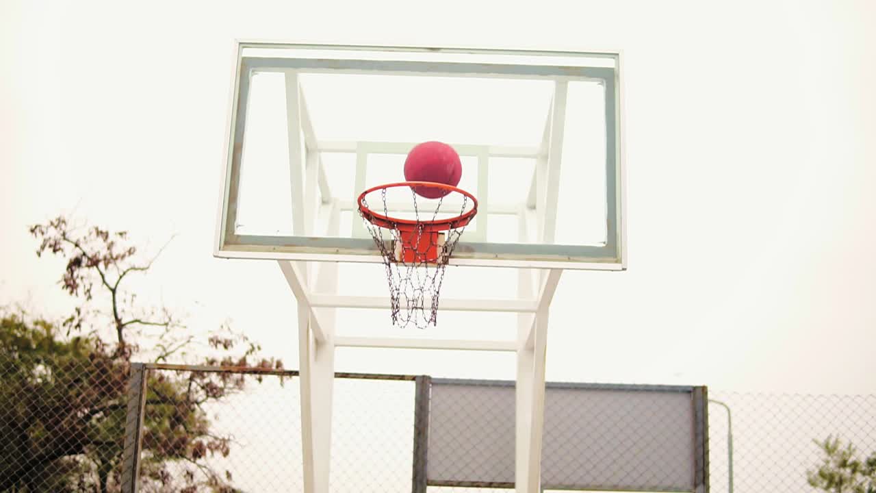 vista retrospectiva de un joven jugando al baloncesto: está saltando y lanzando una pelota a la canasta con éxito. disparo en cámara lenta
