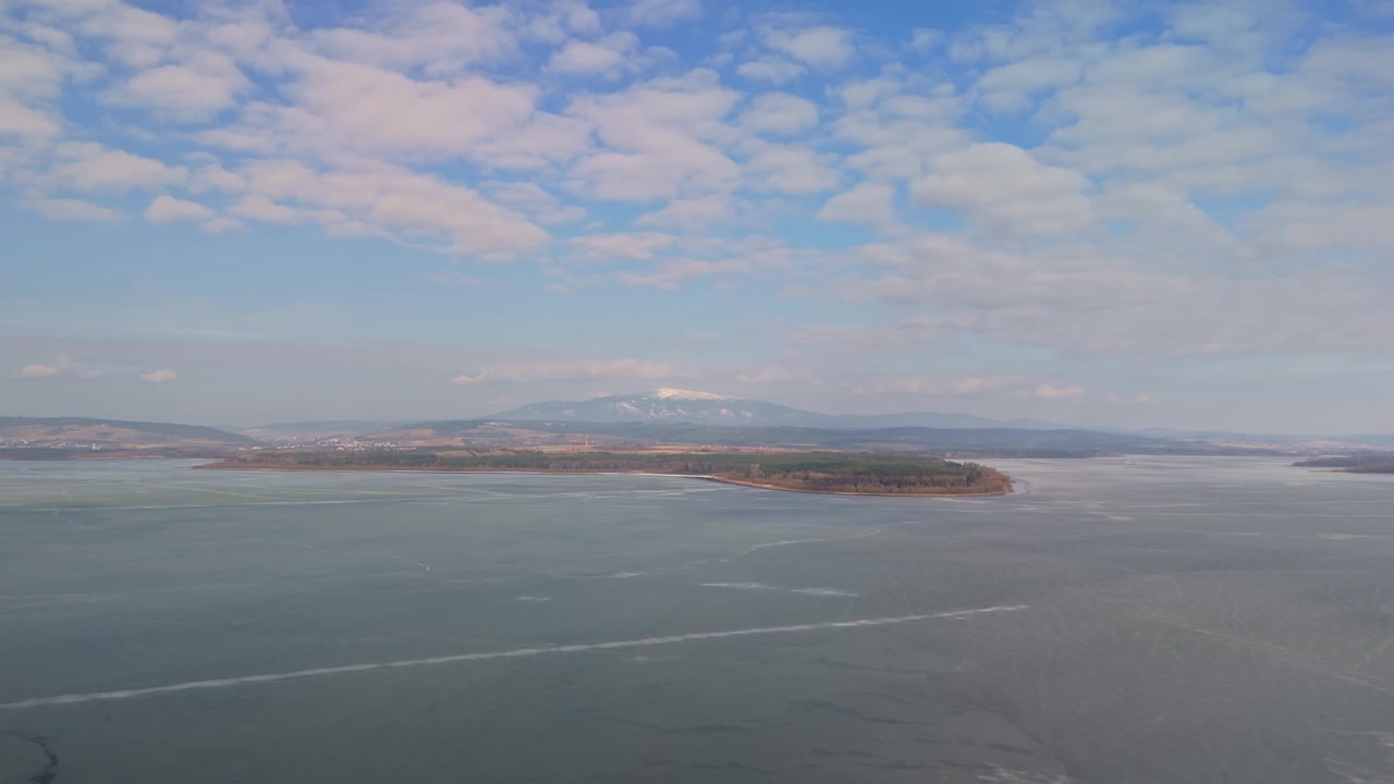 スロバキア北部のオラヴァ貯水池。雪をかぶった山々や森林に覆われた丘に囲まれた凍った湖と、人里離れた冬の風景が広角の空撮で捉えられている。