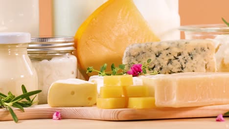 a variety of cheeses and dairy products arranged on a wooden board with herbs and flowers.