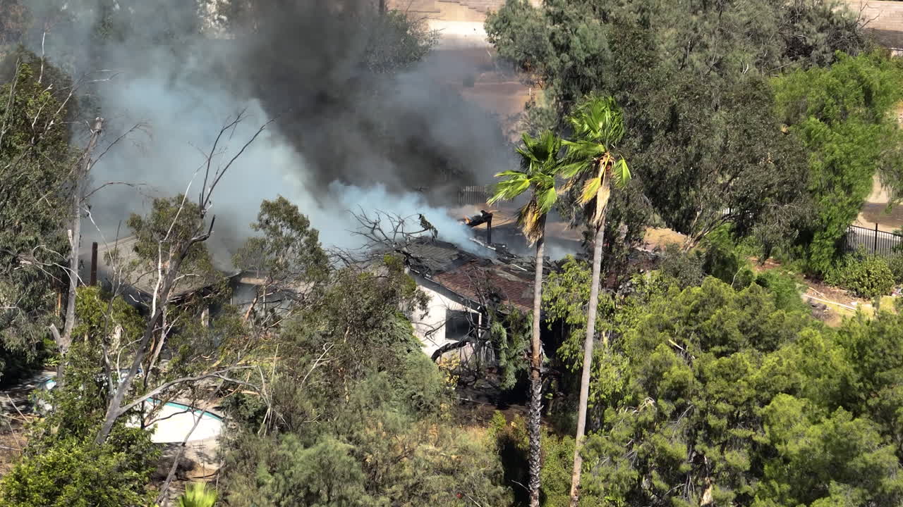 Telephoto drone shot approaching a house fire in Los Angeles, sunny day in USA