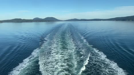 seascape view of a ferry's foam trace in calm ocean water, with mountains in the background