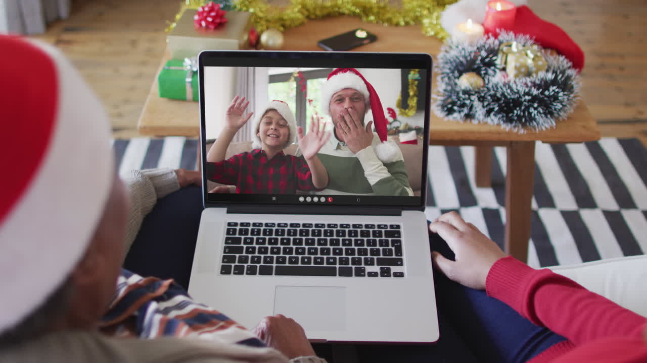 madre y hija afroamericanas usando una computadora portátil para una videollamada de navidad con la familia en la pantalla