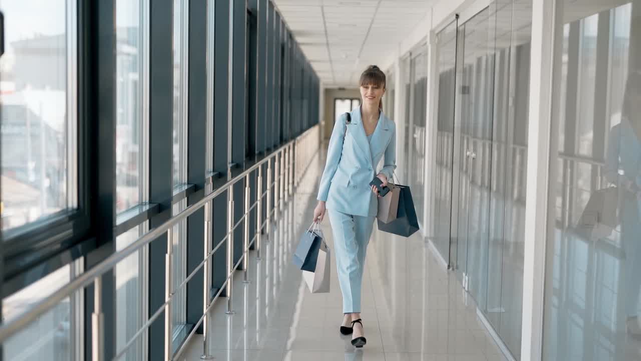 Stylish young girl with packages walks down the glass corridor and smiles