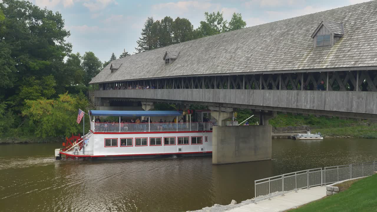A tourist river boat travels under the Bavarian Inn Holz Br&uuml;cke Covered Bridge on the Cass River on a late summer day