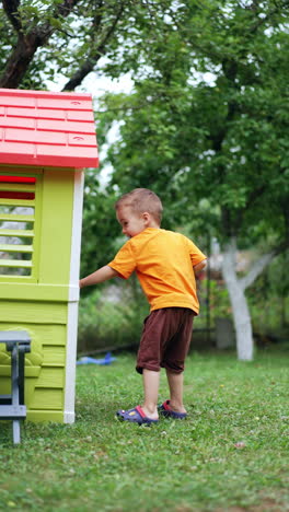 adorable caucasian toddler peeps out of a plastic playhouse. kid leaves the house, closes the door and runs away. vertical video.