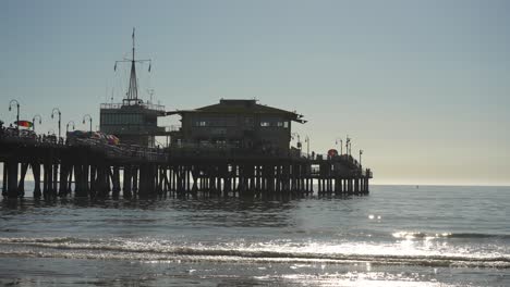 Silueta-De-Un-Muelle-Ocupado-Con-Restaurante-Y-Vista-Al-Mar-Con-Suaves-Olas-En-La-Playa