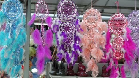 una filmación estacionaria de una tarde ventosa con atrapasueños colgantes con plumas gruesas, varios colores y tamaños que se cuelgan para la venta