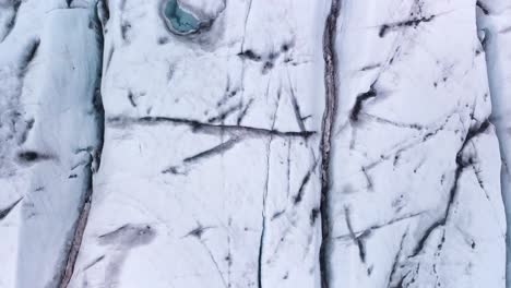 parallel crevasses and glacial blue lake revealed on top-down drone aerial slowly flying over a glacier in iceland