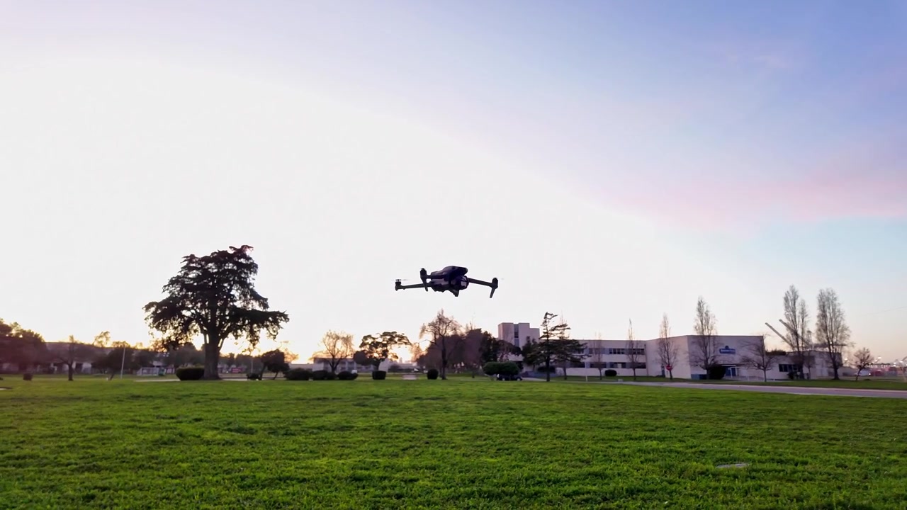 Un drone con telecamera con eliche che girano rapidamente mentre si libra e sale in aria sopra un campo verde al tramonto, mostrando la moderna tecnologia aerea senza pilota e la sorveglianza