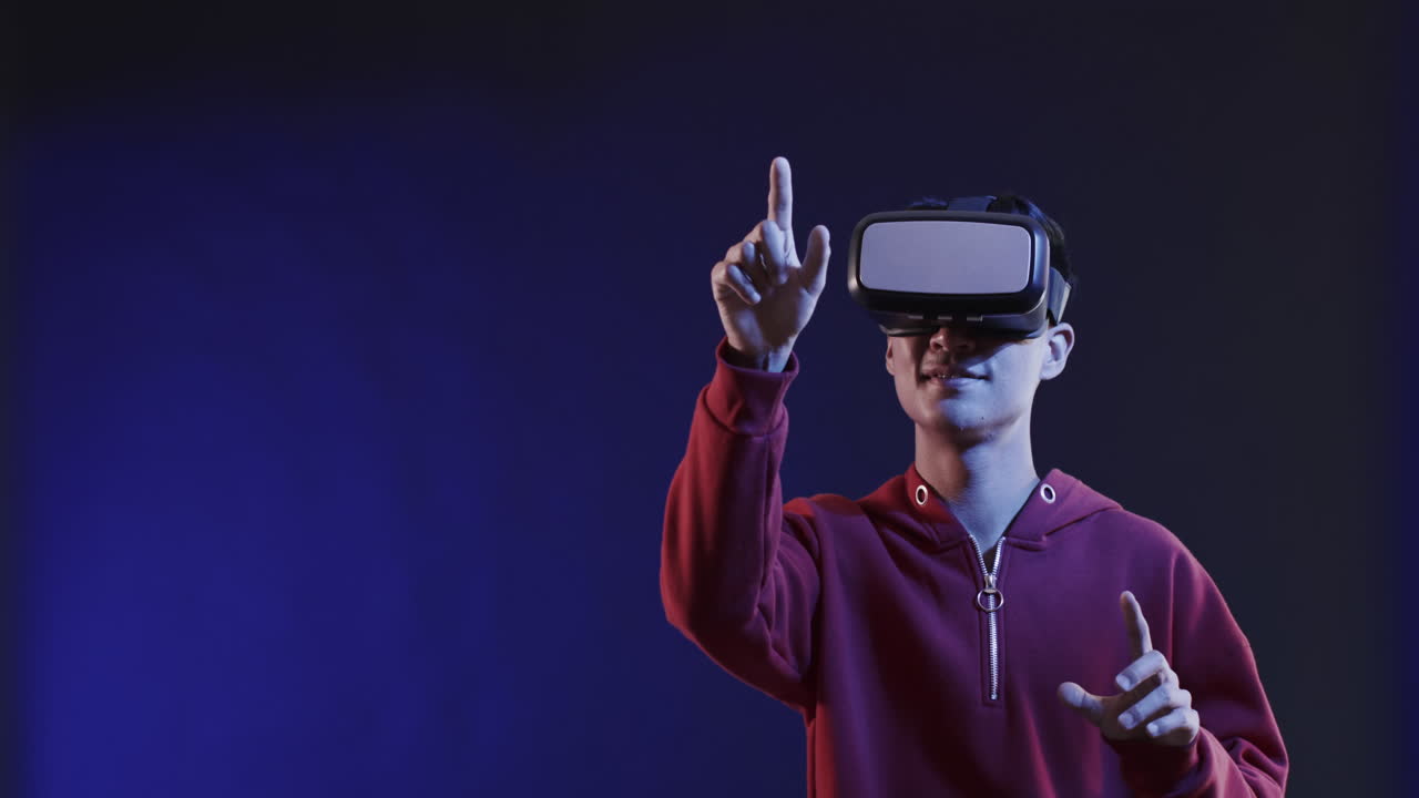 Asian man using vr headset, touching virtual screen on blue background, copy space, slow motion