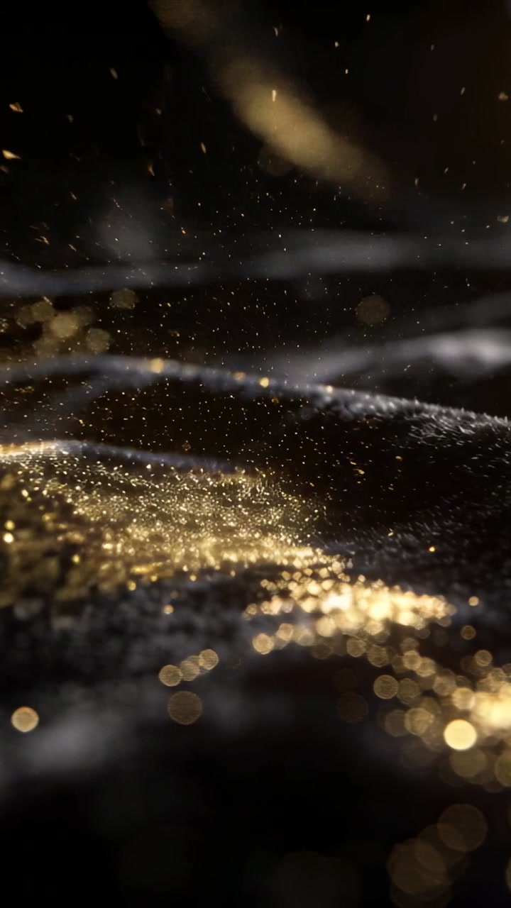 Vertical video: Reacting to tap, dark velvet surface releasing gold dust in macro bokeh warm light