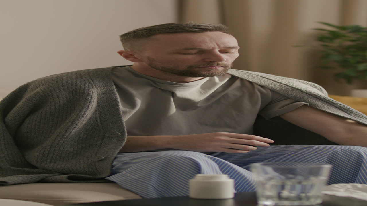Nemocný muž si doma měří teplotu a kašle.