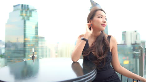 옥상 바에 앉아 있는 동안 바람이 검은 칵테일 드레스를 입은 아름다운 젊은 여성의 머리카락을 흩뿌린다