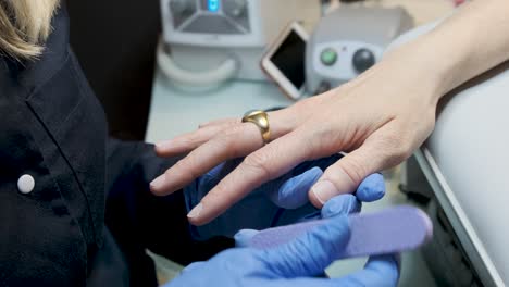 mujer en un salón de uñas recibiendo una manicura por una esteticista con una lima de uñas