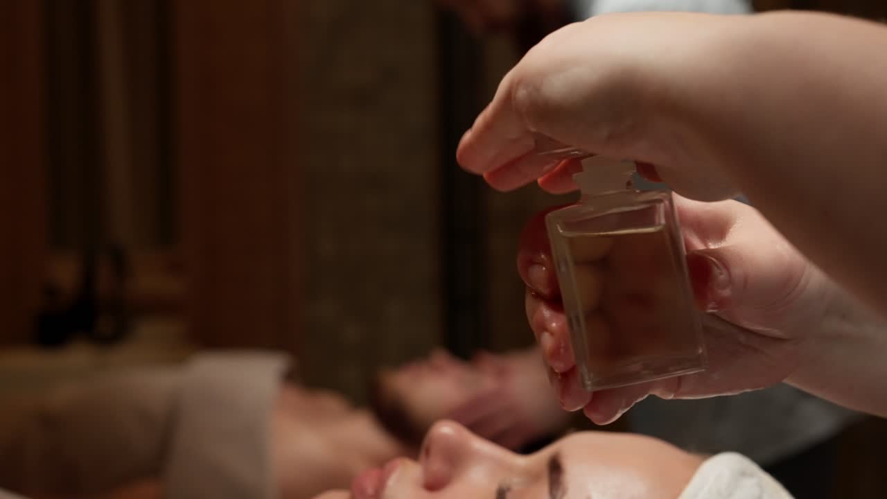 Hænder holder og åbner en lille flaske massageolie i et spa
