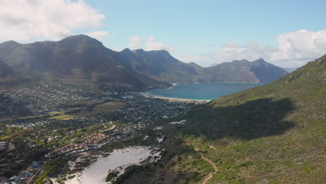 overlooking the harbor town of hout bay surrounded by mountains and the hout bay beach in the distance in cape town, south africa - wide angle aerial shot