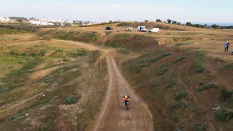 aerial dolly tracking shot of a motorcyclist on a dusty motocross track in malaga in spain with dusty path and people watching the stunts of the motocross rider on the hills