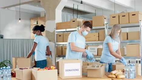 grupo multiétnico de voluntarios en cajas de embalaje de máscaras faciales con comida y ropa en almacén de caridad