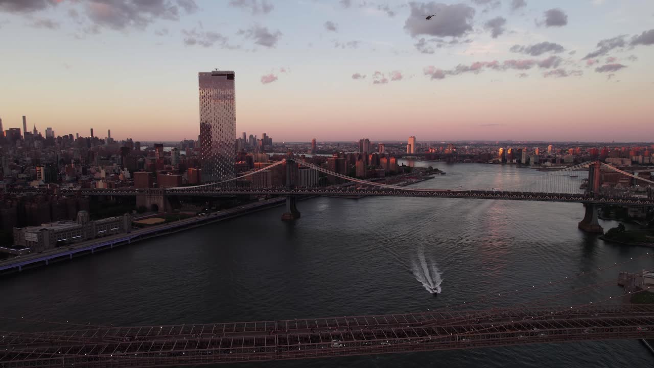 Aerial view of a boat driving under the Manhattan and the Brooklyn bridges, sunset in NYC, USA
