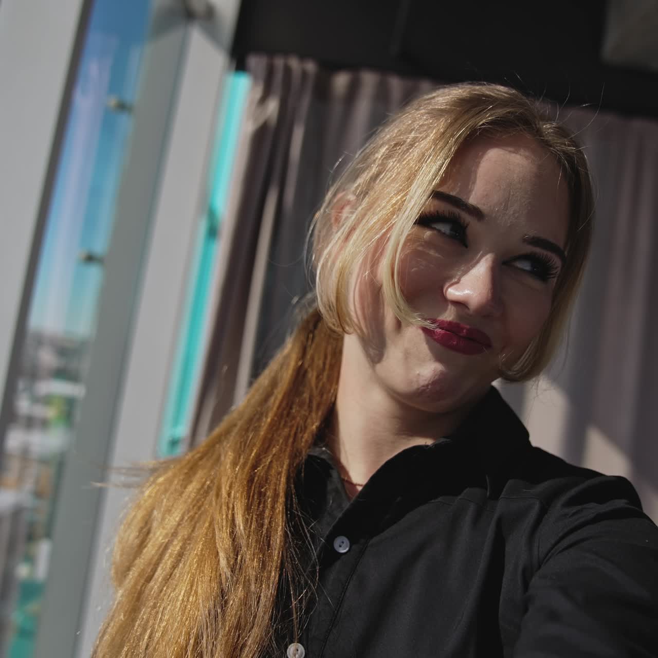 Smiling red-haired young adult lady takes selfie. Big-eyed pretty woman steps back before the camera. Close up