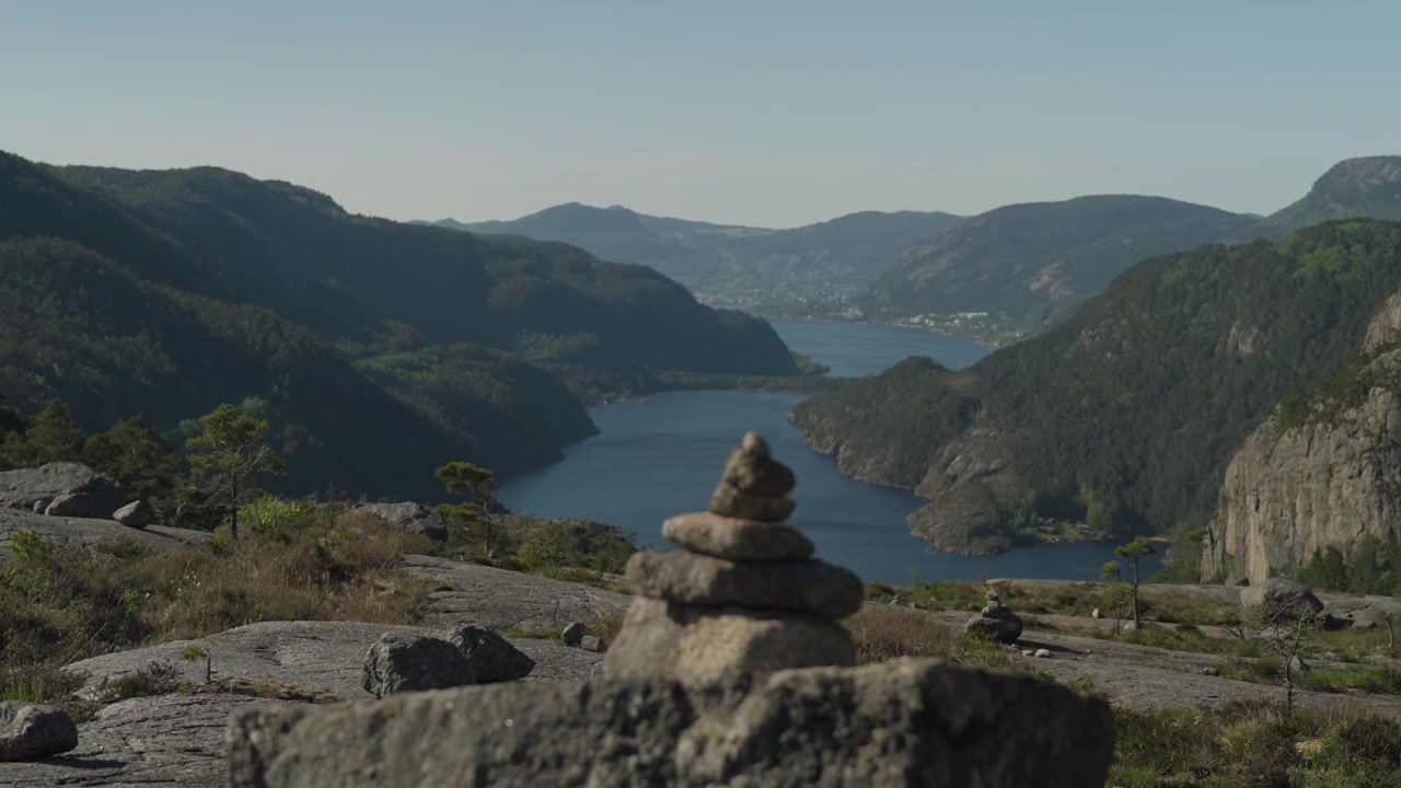 Natursköna bilder och närbild av ett stenröse centrerat ovanför Lysefjorden i Norge under en klarblå sommarhimmel, som fångar fridfulla nordiska landskap och naturlig skönhet