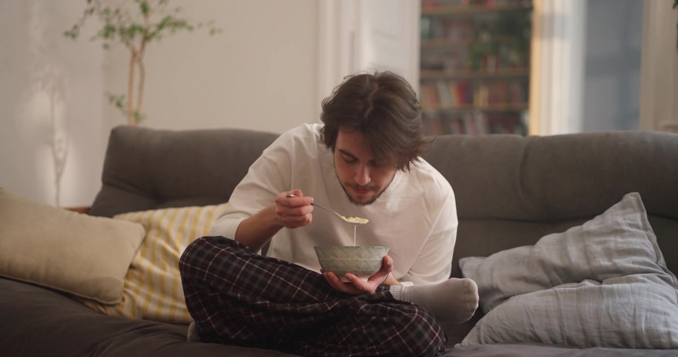 Giovane uomo che mangia cereali sul divano di casa
