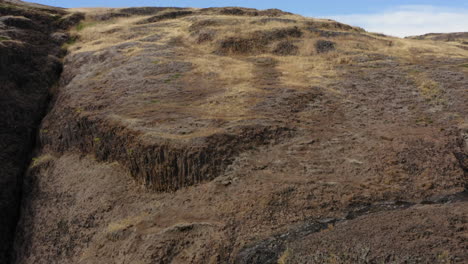 Lowering-down-a-cliff-with-small-waterfall-on-sunny-day,-aerial