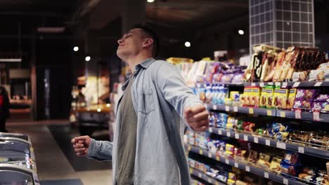 At-the-supermarket:-Happy-stylish-man-with-dances-freely-in-big-shopping-mall-in-front-the-shelves-with-goods.-Positive-dances