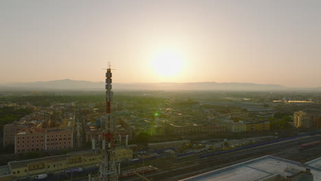 Aerial-panoramic-view-of-buildings-in-borough-at-sunrise.-Forwards-fly-around-telecommunication-antenna-and-railway-tracks.-Rome,-Italy