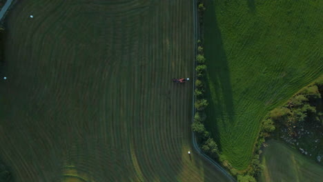 Vista-Aérea-De-Una-Empacadora-Que-Hace-Rollos-De-Pacas-De-Heno-En-Tierras-De-Cultivo-Verdes,-Noruega