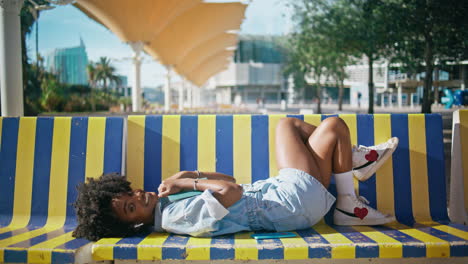 relaxed student resting campus with textbook. girl lying on bench holding book.