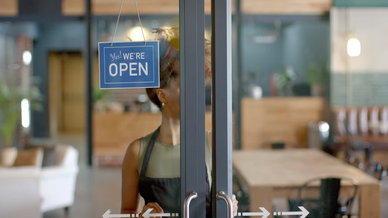 Cafémitarbeiter greift nach oben, dreht das 'Geschlossen'-Schild auf 'Offen' und öffnet die Tür, um Kunden zu empfangen.
