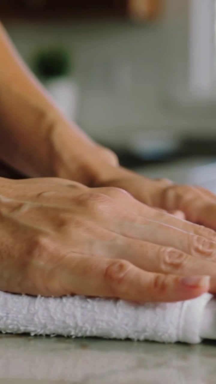 Video verticale: Mani che si avvicinano, sistemano, premono e lisciano un asciugamano sul bancone della cucina per piegarlo.