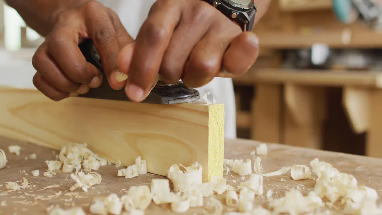 Close up of male carpenter's hands planing a plank of wood with a hand plane in a carpentry shop