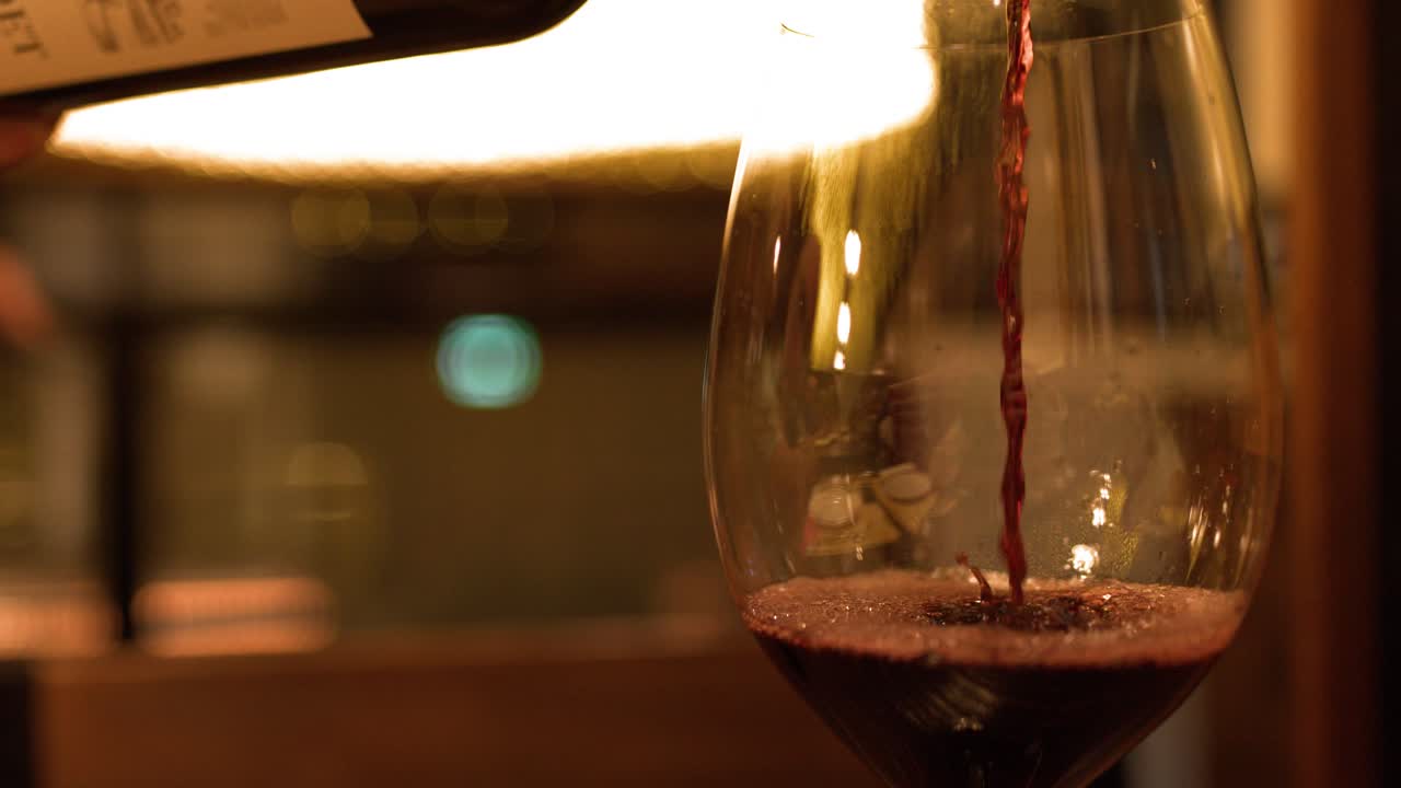 Uno scatto ravvicinato cattura il versamento di vino rosso in un bicchiere in un ristorante scarsamente illuminato