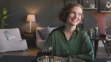 retrato de una mujer bonita sonriente sentada en la mesa de la cena, hablando y luego brindando a la cámara con una copa de vino tinto