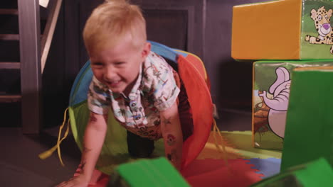 young happy boy crawling through a soft play tunnel