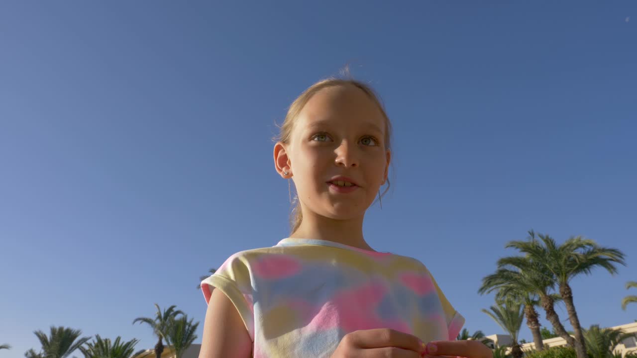 retrato de una adolescente hablando con alguien en el cielo azul y el fondo de la palmera. disparo de mano de bajo ángulo