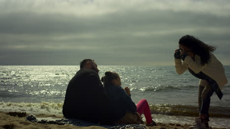 la familia feliz tomando fotos en la playa del océano. la gente sentada posando la cámara por el mar.