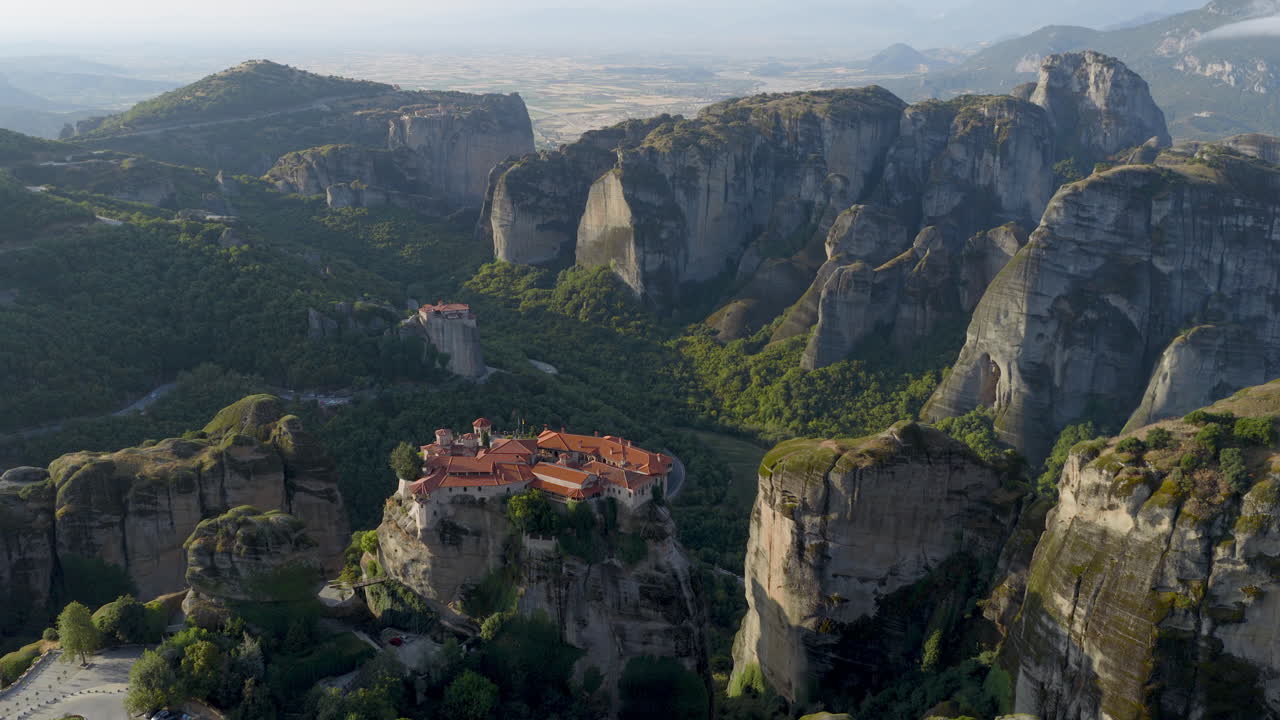 Cinematic aerial view of Meteora monastery in Greece perched on towering cliffs, dramatic rock formations and lush green valley create a breathtaking historic scene