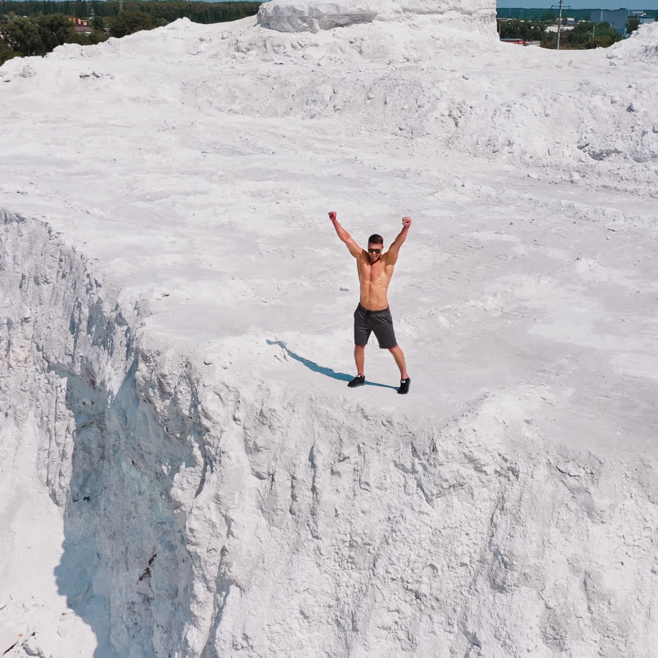 Happy sportsman on natural background. Muscular athlete raises his arms while standing on rocky hill in the countryside.