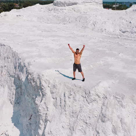 happy sportsman on natural background. muscular athlete raises his arms while standing on rocky hill in the countryside.