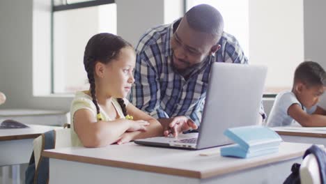 video of happy african american male teacher helping caucasian girl with laptop