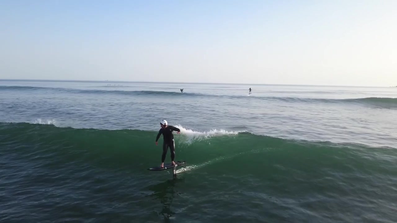 Vista aérea de un rider de hidroala generando velocidad mediante bombeo, deslizándose sobre el océano con equilibrio, control y técnica de foil avanzada