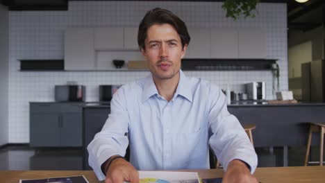 hombre de negocios caucásico teniendo video chat pasando por el papeleo en la cocina del lugar de trabajo