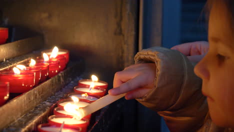 detail of a beautiful blonde little girl lighting candles carefully in a church and then blowing them