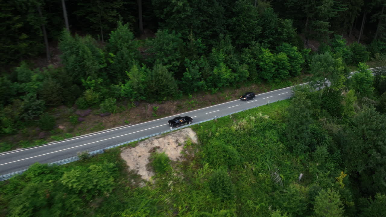 Vista aerea che segue un'auto sportiva d'epoca su una strada forestale, giornata cupa