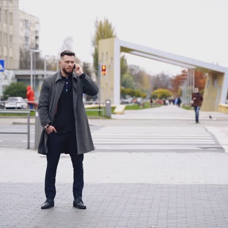 portrait of a man having a phone talk outdoors. handsome businessman in suit and warm coat stands on the city street uses mobile phone. slow motion.