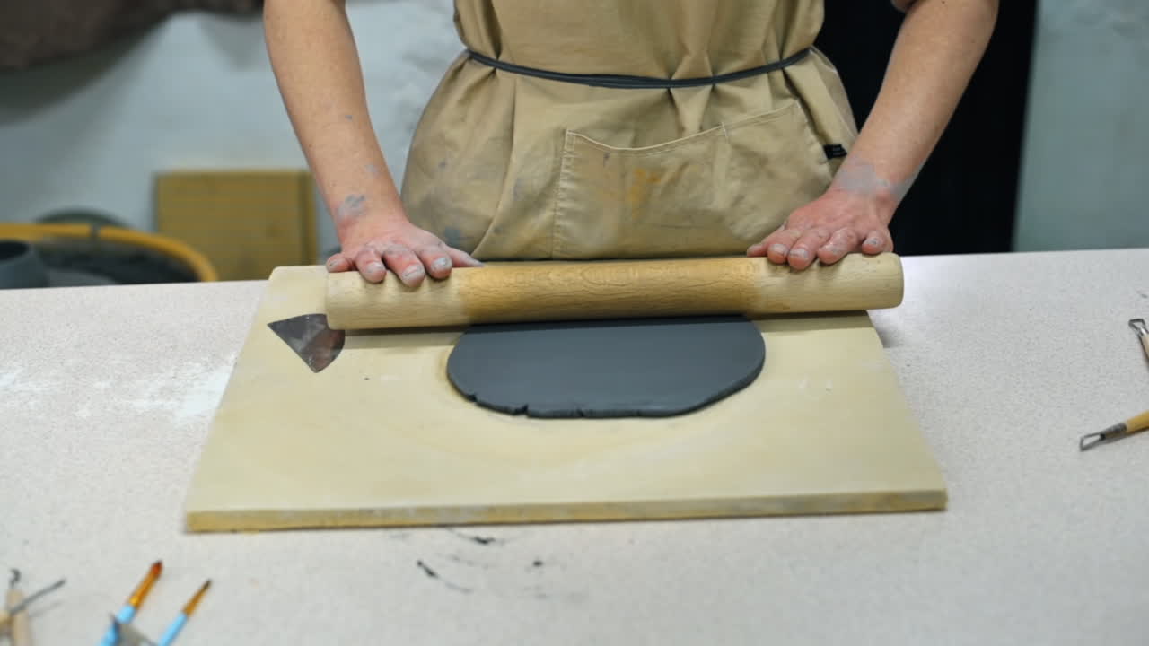 The master of sculpting pottery working in a studio. Rolling out the clay with a rolling pin. Tools on the table. Slow motion