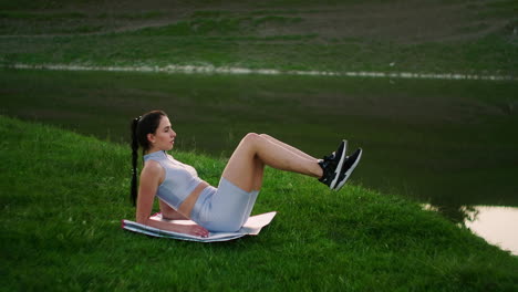 a woman does exercises for the muscles of the press lying on the grass in a park near the lake. work with abs muscles. creating a beautiful body